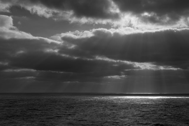 Sunbeams illuminating sea through dark rain clouds creating dramatic and tranquil scene. Perfect for concepts related to nature, weather, serenity, or inspiration. Ideal for websites, blogs, and articles focusing on weather phenomena or the beauty of nature.