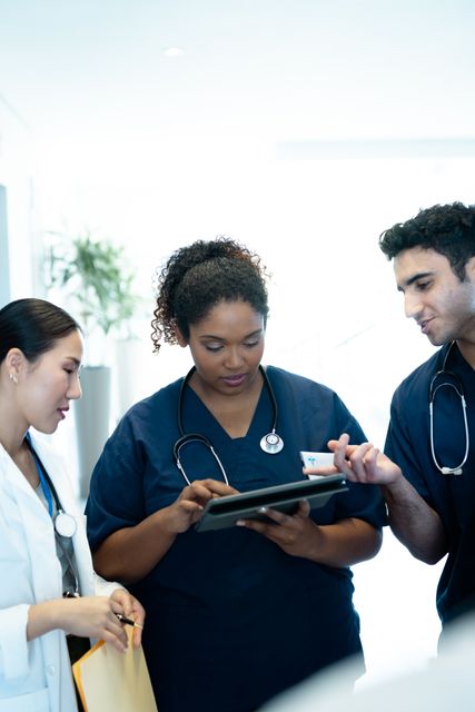 Three diverse doctors, male and female, discuss over a tablet in a hospital corridor - Download Free Stock Photos Pikwizard.com
