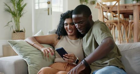 Couple sharing smartphone smiling on sofa with smartwatch in open plan living room