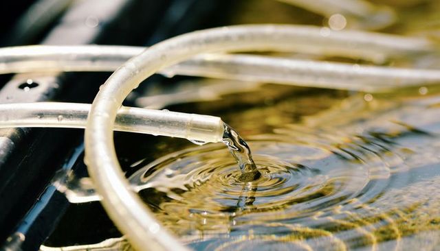 Clear tubing pouring water creating golden ripples in sunlight