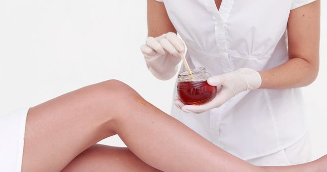A Caucasian beautician prepares to apply wax on a client's leg for hair removal, with copy space. Professional beauty treatments like waxing are popular for achieving smooth, hair-free skin.