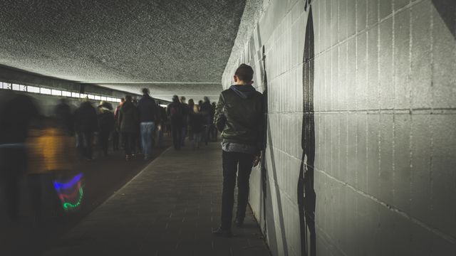 Person is standing against a wall, separated from a crowd. Useful for themes exploring solitude, psychological reflection, or highlighting urban atmospheres. Ideal for articles, blogs on mental health or urban life, and social media posts on personal reflection.