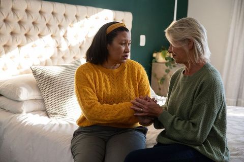 Senior women comforting each other on bed holding hands showing empathy and support