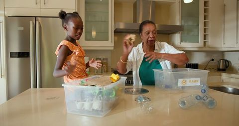 Grandmother and Granddaughter Sorting Recyclables in Kitchen for Eco-education