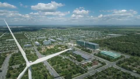 Drone passing wind turbine hub and blade while surveying tech campus and solar roofs