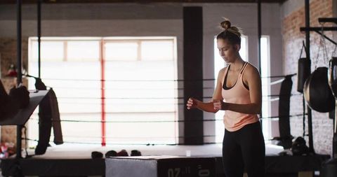 Female athlete adjusting wrist wraps near jump box in boxing gym