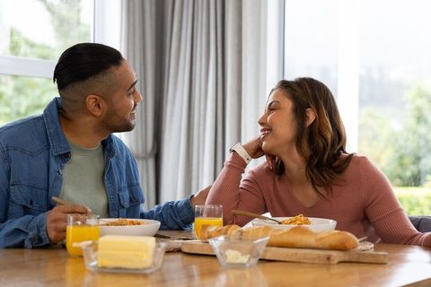 Young couple sharing cozy breakfast at sunlit dining table, smiling and connecting