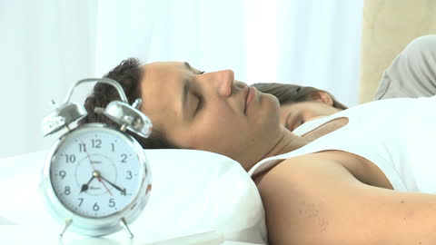 Peaceful Couple Sleeping Next to an Alarm Clock in Bright Bedroom