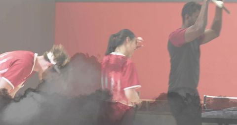 Table tennis trio playing intensely around table, paddles raised, smoke adding motion