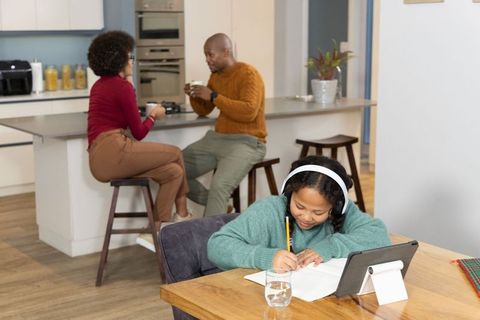 Child doing homework on tablet while parents enjoying coffee in cozy modern kitchen