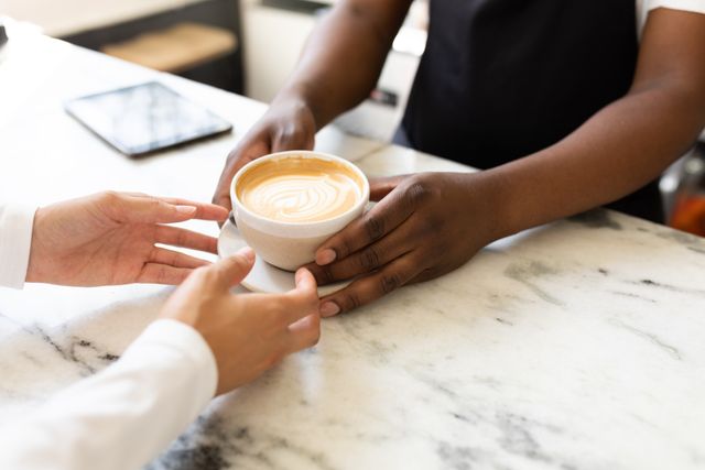 Male african american barista and biracial female customer holding coffee cup at cafe counter. unaltered, cafe culture, people, consumerism and occupation concept.
