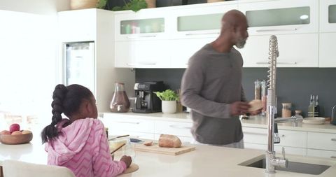 Father and daughter preparing breakfast in bright modern kitchen with bread on island