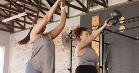 Diverse women lifting kettlebell together in industrial gym for strength and friendship