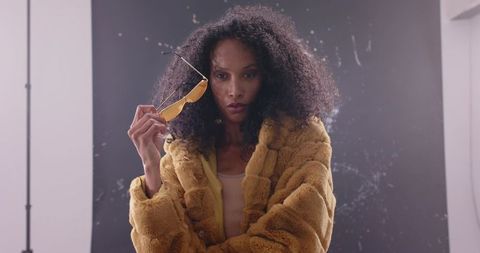 Bold fashion portrait of model wearing mustard faux fur coat and yellow sunglasses