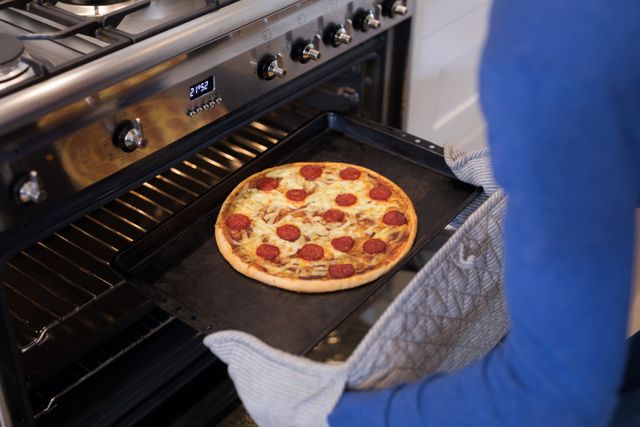 Man putting pizza into oven in kitchen at home