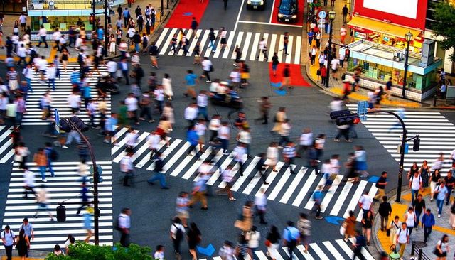Busy urban scramble crossing showing motion-blur pedestrians and diagonal zebra crosswalks