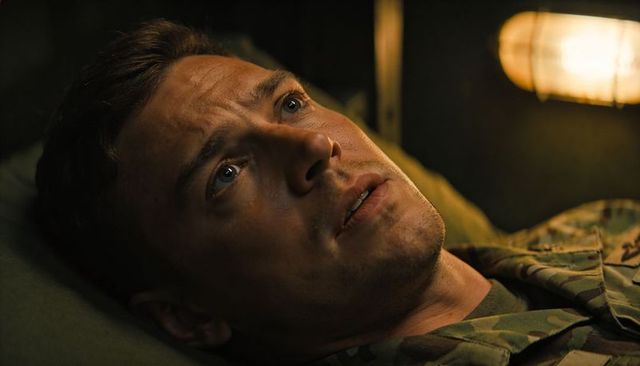 Solitary soldier lying on bunk under caged lamp conveying contemplation and cinematic mood