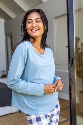 Smiling asian woman wearing light blue top and checkered pajama pants on balcony