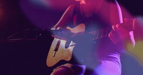 Teen Musician Performing on Dimly Lit Stage with Acoustic Guitar