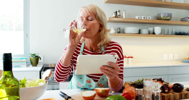 Elderly Woman Cooking and Drinking Wine Using Digital Tablet in Modern Kitchen - Download Free Stock Images Pikwizard.com