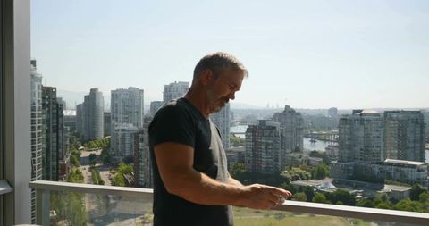 Man relaxing on high-rise balcony using smartphone