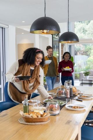 Friends Gathering Around Long Wooden Dining Table in Sunlit Open-Plan Kitchen