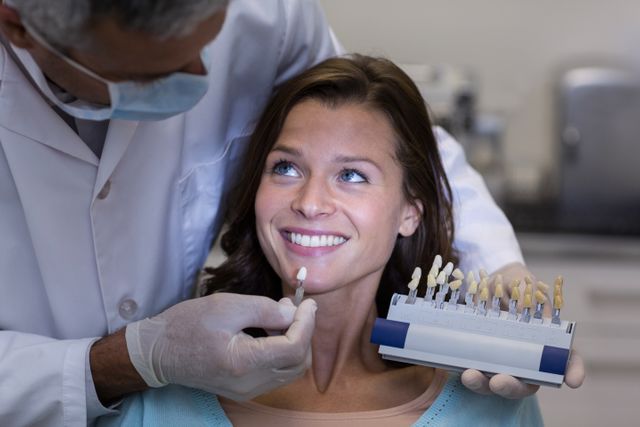 Dentist examining female patient with teeth shades at dental clinic