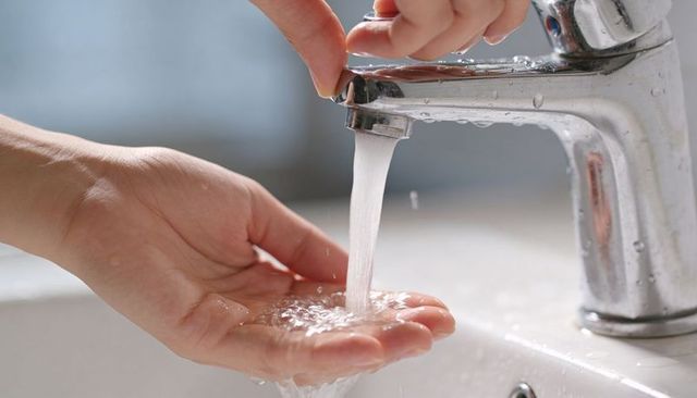 Hands collecting running water from chrome faucet over porcelain sink handwashing hygiene