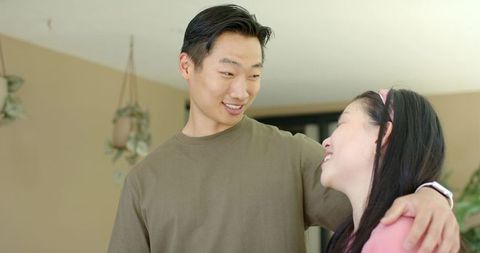 Young asian couple sharing warm smile and gentle embrace at home with hanging plants