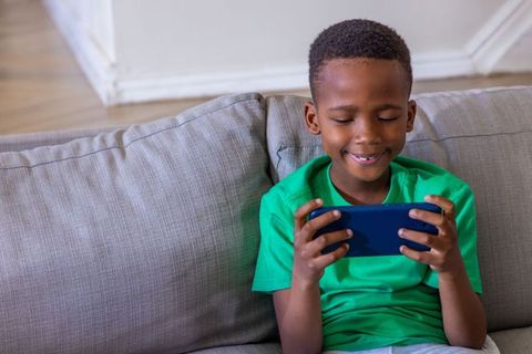 African american boy playing mobile game on sofa smiling and focused at home