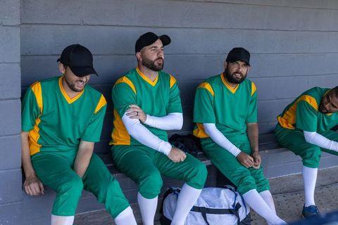 Baseball teammates sitting and resting on dugout bench wearing green and yellow uniforms