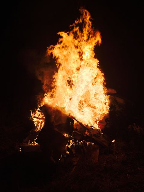 Large bonfire blazing in the darkness, illuminating surrounding area. Ideal for concepts relating to camping, warmth, outdoor gatherings, survival skills, or fire safety.