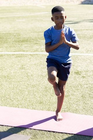 School-age boy practicing tree pose on yoga mat outdoors balancing and meditating