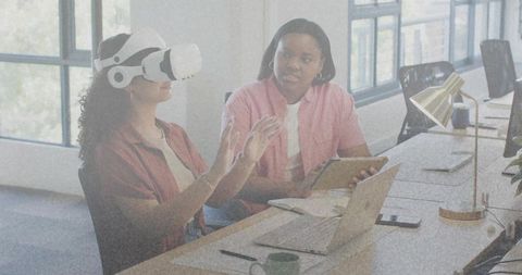 Women coworkers testing virtual reality headset while collaborating over tablet and laptop in office