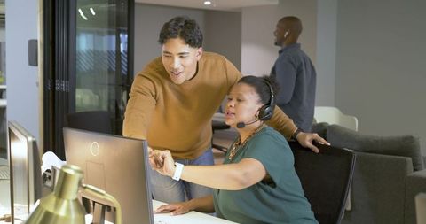 Multicultural team collaborating at workstation with headset and desktop monitors