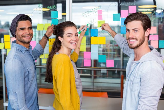 Portrait of smiling executives writing on sticky note on glass wall in office
