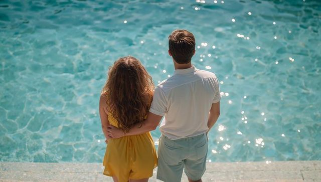Couple standing embracing poolside by turquoise water, sunlit summer romance getaway