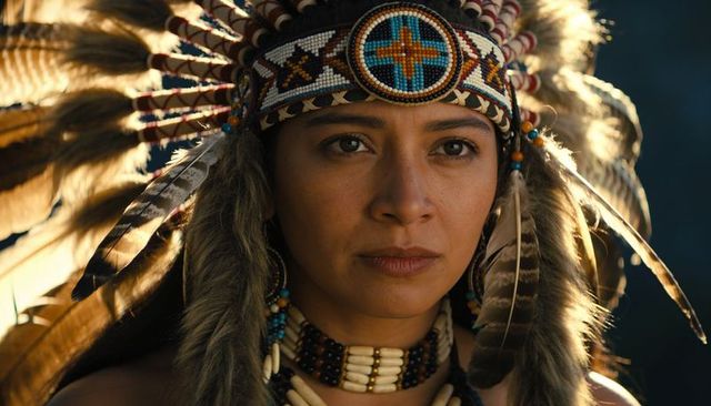 Indigenous-style woman wearing ornate feather headdress and beaded choker closeup