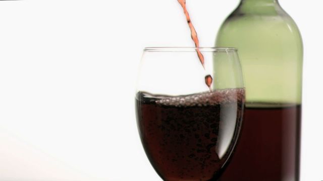 Red wine is shown flowing in a captivating slow motion into a glass, paused to capture the swirling liquid. The green bottle stands partially visible, helping enrich the backdrop. Suitable for use by wine sellers, restaurants, or culinary blogs emphasizing the aesthetics and enjoyment of fine wine. Perfect for illustrating blog entries, marketing materials, or wine tasting event promotions.