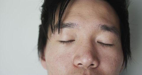 Closeup asian male face with closed eyes showing natural skin texture and soft lighting