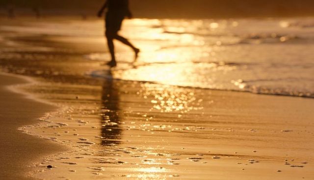 Golden Sunset Beach Walk Reflection Silhouette on Wet Sand with Footprints and Calm Sea