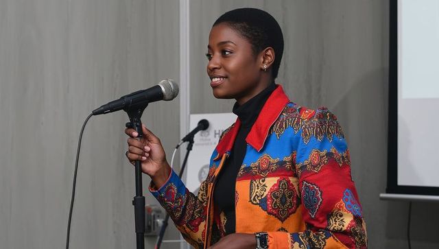 Confident presenter delivering talk wearing colorful patterned blazer speaking at microphone