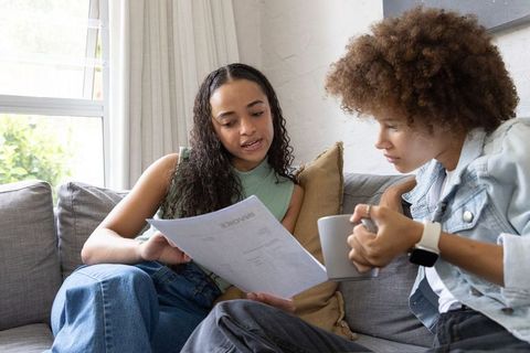 African american women reviewing invoice on couch holding mug discussing home finance