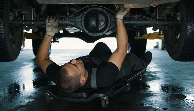 Mechanic lying on creeper repairing rear axle undercarriage in industrial garage workshop