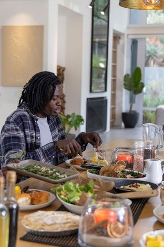 African American man cutting roast chicken at relaxed family dinner in modern home