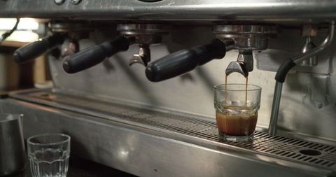 Pulling rich espresso shot into glass with crema on commercial espresso machine counter