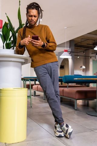 African american male leaning on high table using smartphone in modern coworking lounge