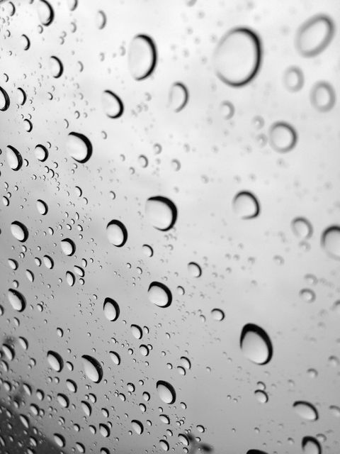 Close-up shot of raindrops on a glass window during a rainy, overcast day. Varying sizes of water droplets create an abstract pattern. Useful for backgrounds, weather-related articles, or designs emphasizing nature’s simplicity and tranquility.
