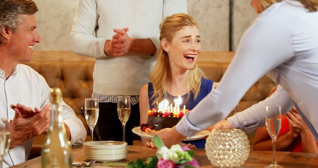 A young Caucasian woman is delighted as she is presented with a birthday cake by friends or family at a celebration, with copy space. Joy and surprise are evident on her face, capturing a moment of personal happiness during a social gathering.