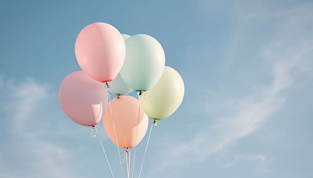 Pastel helium balloons floating against soft blue sky with copy space for celebrations